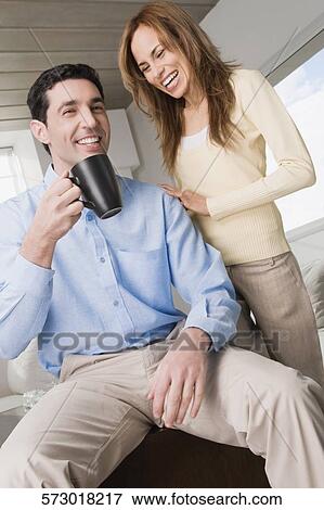 Mid adult man holding a coffee cup and a mid adult woman laughing beside him View Large Photo Image Stock Photo - Mid adult man holding a coffee cup and a mid adult woman laughing beside him. Fotosearch