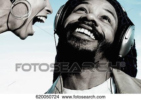 Picture - Mid adult man listening to music and a young woman shouting in front of him. Fotosearch