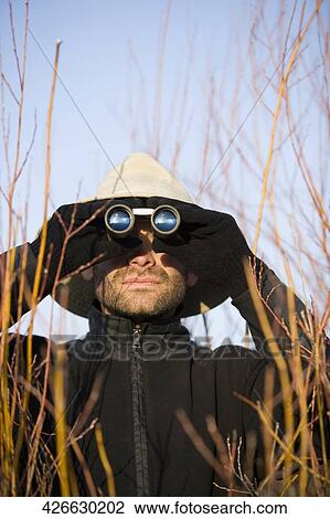 Mid adult man looking through binoculars in a forest View Large Photo Image Stock Image - Mid adult man looking through binoculars in a forest. Fotosearch