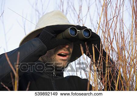 Mid adult man looking through binoculars in a forest View Large Photo Image Stock Photo - Mid adult man looking through binoculars in a forest. Fotosearch