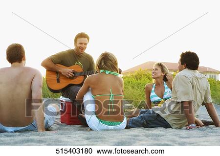 Mid adult man playing a guitar and his friends sitting around him View Large Photo Image Stock Image - Mid adult man playing a guitar and his friends sitting around him. Fotosearch