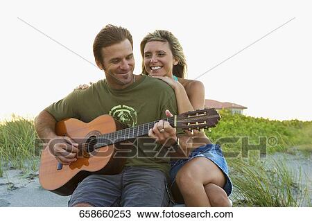 Stock Image - Mid adult man playing a guitar with a young woman smiling. Fotosearch