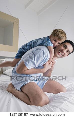 Mid adult man playing with his son on the bed View Large Photo Image Stock Photo - Mid adult man playing with his son on the bed. Fotosearch