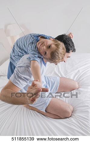 Mid adult man playing with his son on the bed View Large Photo Image Stock Photo - Mid adult man playing with his son on the bed. Fotosearch