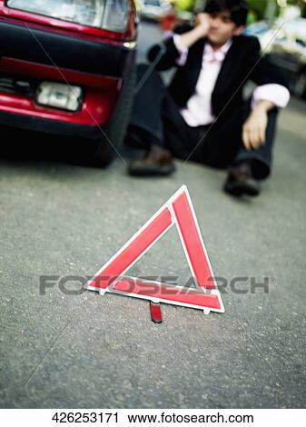 Mid adult man sitting by a broken-down car behind a warning triangle on the road View Large Photo Image Stock Image - Mid adult man sitting by a broken-down car behind a warning triangle on the road. Fotosearch