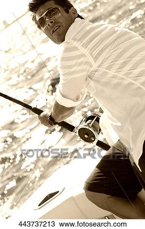 Stock Image - Mid adult man sitting in a boat and fishing. Fotosearch