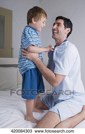 Mid adult man smiling with his son on the bed View Large Photo Image Stock Image - Mid adult man smiling with his son on the bed. Fotosearch