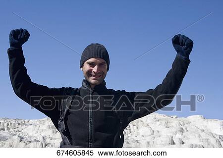 Stock Photography - Mid adult man standing with his arms raised. Fotosearch