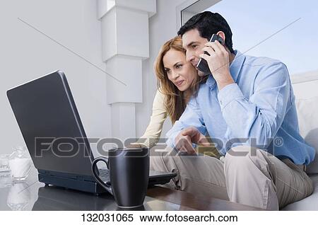 Mid adult man talking on a mobile phone and a mid adult woman working on a laptop View Large Photo Image Stock Photography - Mid adult man talking on a mobile phone and a mid adult woman working on a laptop. Fotosearch