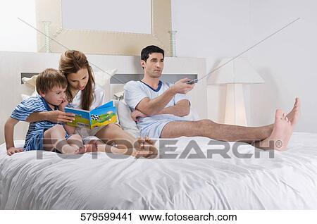 Mid adult man watching tv beside his wife and son on the bed View Large Photo Image Stock Image - Mid adult man watching tv beside his wife and son on the bed. Fotosearch