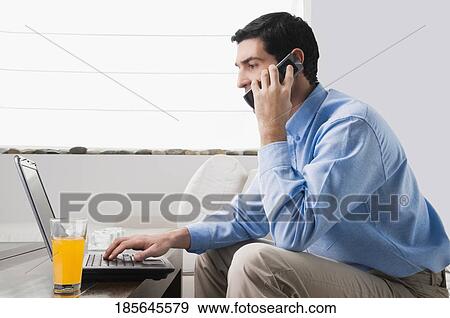 Mid adult man working on a laptop and talking on a mobile phone View Large Photo Image Stock Photo - Mid adult man working on a laptop and talking on a mobile phone. Fotosearch