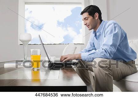 Mid adult man working on a laptop with a glass of juice on the table View Large Photo Image Stock Photograph - Mid adult man working on a laptop with a glass of juice on the table. Fotosearch
