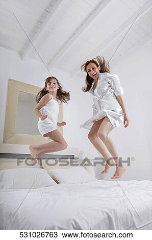 Mid adult woman jumping with her daughter on the bed View Large Photo Image Stock Image - Mid adult woman jumping with her daughter on the bed. Fotosearch