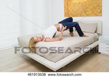 Mid adult woman putting on jeans on the bed View Large Photo Image Stock Photo - Mid adult woman putting on jeans on the bed. Fotosearch
