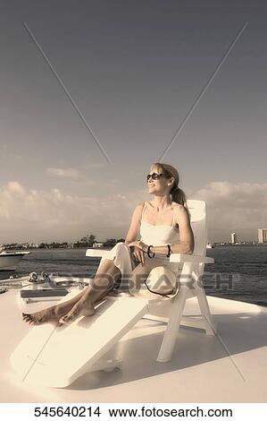Picture - Mid adult woman resting on a deck chair and smiling. Fotosearch