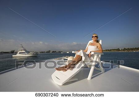 Stock Image - Mid adult woman resting on a deck chair and smiling. Fotosearch