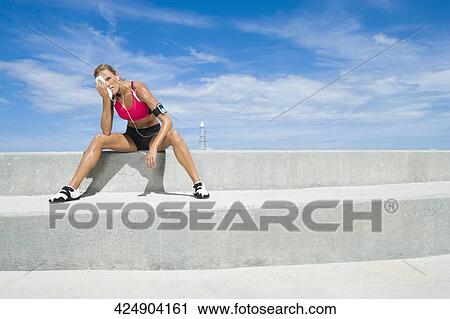 Stock Image - Mid adult woman sitting on a ledge. Fotosearch