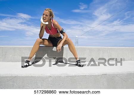 Stock Image - Mid adult woman sitting on a ledge. Fotosearch