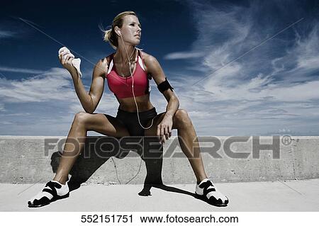 Stock Image - Mid adult woman sitting on a ledge. Fotosearch