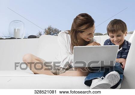 Mid adult woman smiling with her son in front of a laptop View Large Photo Image Stock Image - Mid adult woman smiling with her son in front of a laptop. Fotosearch