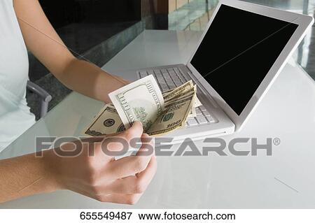 Stock Photo - Mid section view of a businesswoman counting paper currency in front of a laptop. Fotosearch