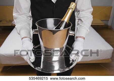 Mid section view of a waiter holding a champagne bottle in an ice bucket View Large Photo Image Stock Photography - Mid section view of a waiter holding a champagne bottle in an ice bucket. Fotosearch