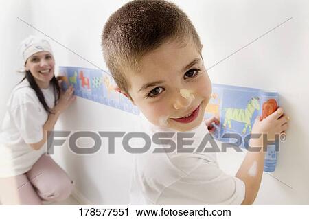 Stock Image - Portrait of a boy and his mother pasting wallpaper. Fotosearch