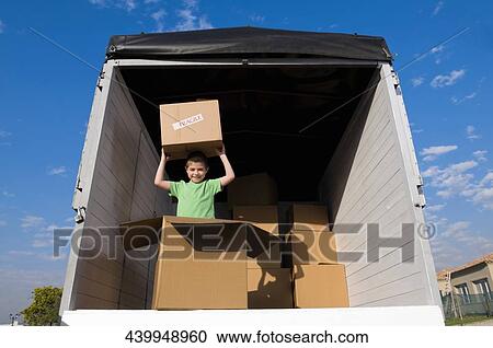 Stock Image - Portrait of a boy carrying a cardboard box and smiling. Fotosearch