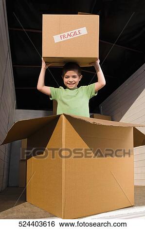 Stock Photograph - Portrait of a boy carrying a cardboard box and smiling. Fotosearch