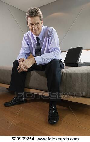 Picture - Portrait of a businessman sitting on the bed and smiling. Fotosearch
