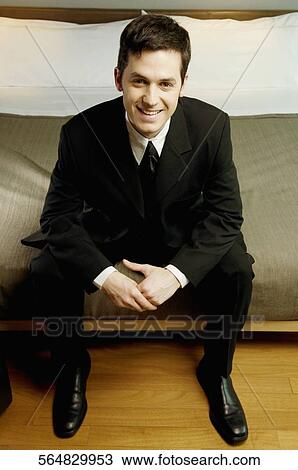 Stock Image - Portrait of a businessman sitting on the bed and smiling. Fotosearch