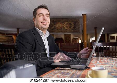 Portrait of a businessman using a laptop at a restaurant and smiling View Large Photo Image Stock Photo - Portrait of a businessman using a laptop at a restaurant and smiling. Fotosearch