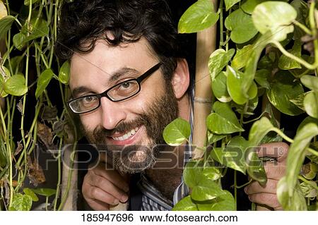 Portrait of a mature man peeking through plants and smiling View Large Photo Image Stock Photograph - Portrait of a mature man peeking through plants and smiling. Fotosearch