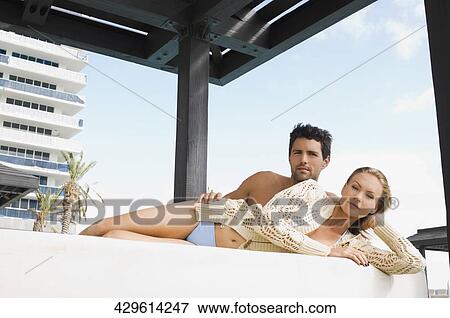 Stock Photo - Portrait of a mid adult couple resting at the poolside. Fotosearch