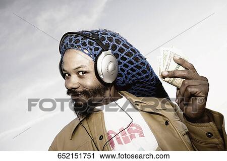 Stock Image - Portrait of a mid adult man listening to music and holding banknotes. Fotosearch