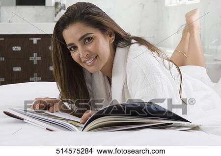 Picture - Portrait of a mid adult woman lying on the bed and reading a book. Fotosearch