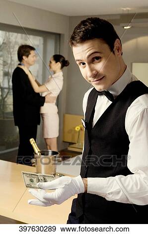 Stock Photo - Portrait of a waiter holding US paper currency and smiling. Fotosearch