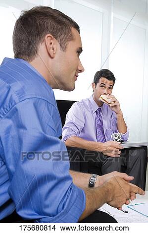 Portrait of a young man eating sandwich and a mid adult man sitting with him View Large Photo Image Picture - Portrait of a young man eating sandwich and a mid adult man sitting with him. Fotosearch
