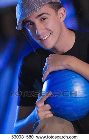 Stock Image - Portrait of a young man holding a bowling ball. Fotosearch