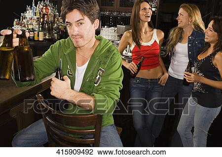 Portrait of a young man holding beer bottles at a bar counter with his three friends standing behind him View Large Photo Image Stock Image - Portrait of a young man holding beer bottles at a bar counter with his three friends standing behind him. Fotosearch