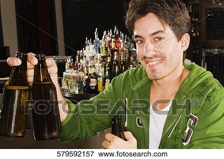 Portrait of a young man holding beer bottles at a bar counter and smiling View Large Photo Image Stock Photo - Portrait of a young man holding beer bottles at a bar counter and smiling. Fotosearch