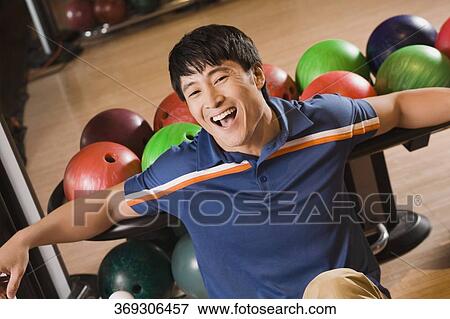 Stock Photo - Portrait of a young man laughing with bowling balls behind him. Fotosearch