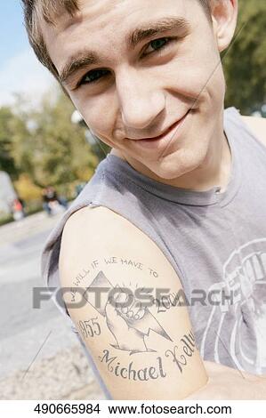 Portrait of a young man showing a tattoo on his arm View Large Photo Image Picture - Portrait of a young man showing a tattoo on his arm. Fotosearch