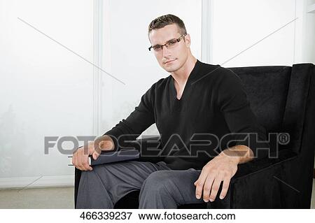 Portrait of a young man sitting in an armchair and holding a book View Large Photo Image Stock Photo - Portrait of a young man sitting in an armchair and holding a book. Fotosearch