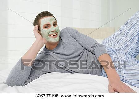 Stock Photo - Portrait of a young man wearing clay facial mask and smiling. Fotosearch