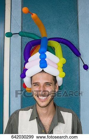 Stock Photo - Portrait of a young man wearing balloons headdress and smiling. Fotosearch