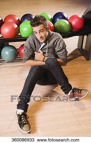 Stock Image - Portrait of a young man with bowling balls in the background. Fotosearch