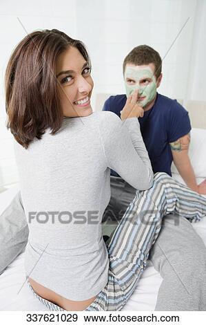 Stock Photo - Portrait of a young woman applying facial mask on a young man's face. Fotosearch