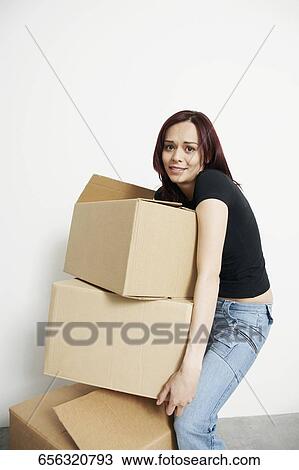 Stock Image - Portrait of a young woman carrying a stack of cardboard boxes. Fotosearch