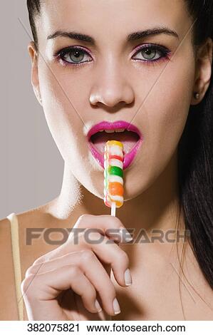 Stock Image - Portrait of a young woman eating a lollipop. Fotosearch